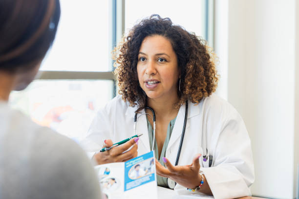 Female doctor discusses healthcare with patient A serious female doctor gestures as she discusses healthcare options with a mature female patient. The patient is reading an informational brochure. consult with your doctor stock pictures, royalty-free photos & images