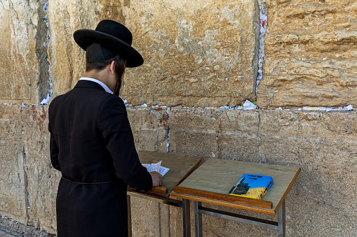 JERUSALEM, ISRAEL - JULY 14, 2019: Jewish orthodox man in traditional black wear praying at Wailing Wall (aka Kotel) - ancient wall in Old City of Jerusalem, one of the most sacred place in Judaism.
