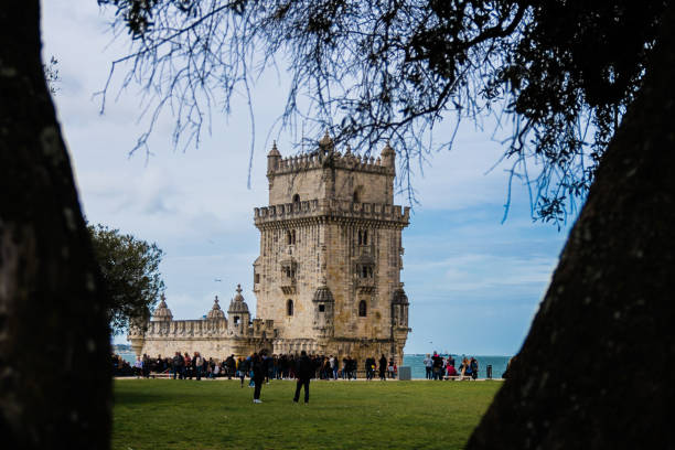 Lisbon , Portugal; 08 April 2018: Belem Tower framed by two trees with several people in the gardens