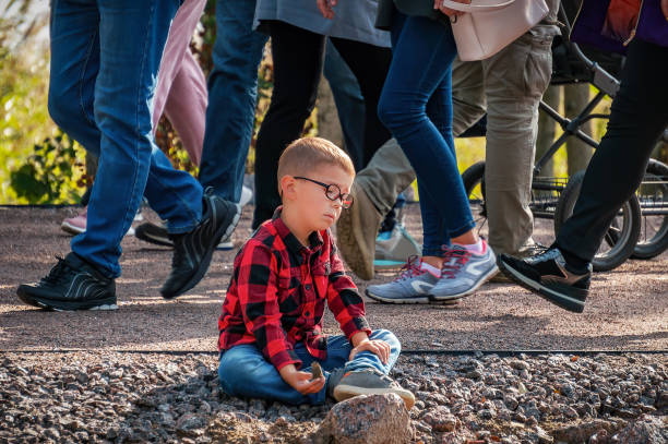 A little sad upset boy with glasses is sitting on the ground, he stock photo