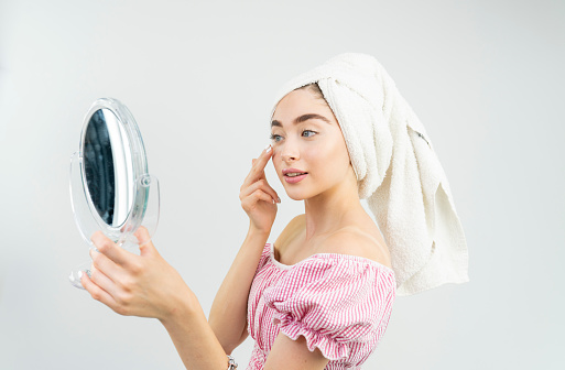 Attractive blonde blue eyed young woman after shower is standing in front of mirror. Women care.