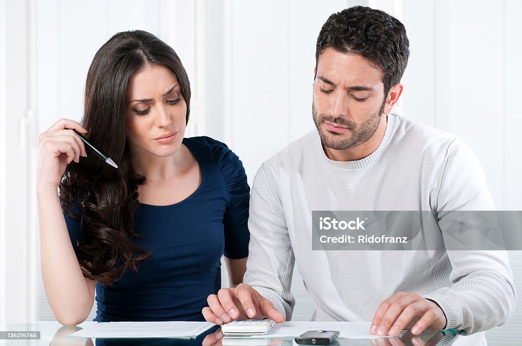 A young couple looking at a calculator and papers Young worried couple looking at their bills and home finance at home. Worried Stock Photo