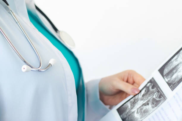聴診器を持つ白い医療コートを着た女性医師は、彼女の手に超音波スキャンの結果を保持します。入院中の看護師。ヘルスケアの概念 - lab coat nurse doctor female doctor ストックフォトと画像