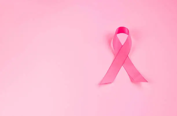 Pink ribbon on colored background. Breast Cancer Awareness Month symbol. Women's health care concept. Promotion of campaign to fight cancer. Copy space.