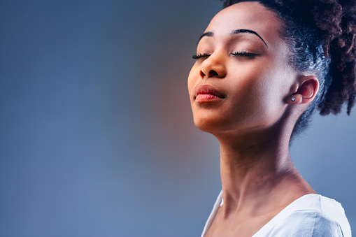 Young Black woman enjoying a quiet moment of quality time with eyes closed and a serene expression in a cropped close up head shot on blue