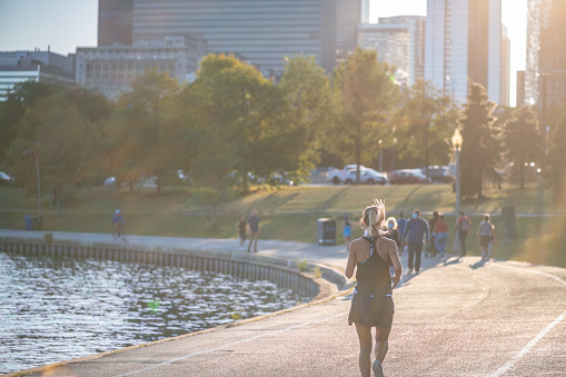 Chicago, IL - September 16, 2021: Light from the setting sun washes over a woman jogging at sunset along the beautiful Lakefront Trail, downtown in the Loop.