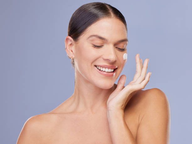 shot of an attractive young woman applying moisturiser against a purple background - cheek color imagens e fotografias de stock