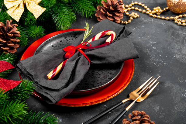istock Christmas table setting concept on a festive table close up. Plate, napkin, candy cane, golden cutlery and christmas decorations on gray background 1342186413