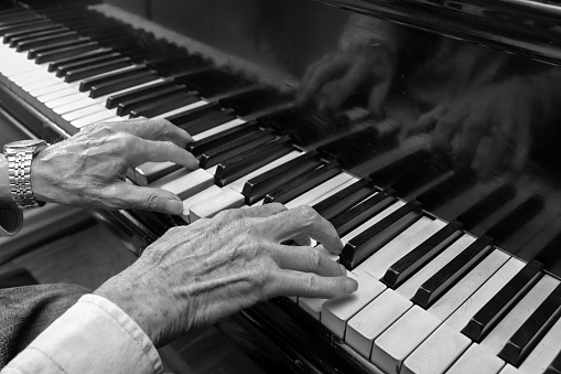 Hands of an old musician playing music on the keyboard of a grand piano, black and white image, concept for culture, art and entertainment, copy space, selected focus, narrow depth of field