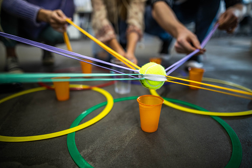 Close up of unrecognizable people playing team building game with tennis ball and disposable cups at casual office.