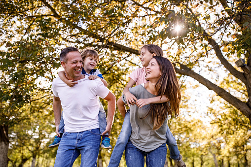 Carefree parents and their small kids having fun while piggybacking in springtime at the park.