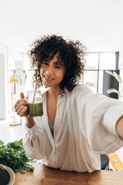 mujer de raza mixta se toma selfie y toma jugo verde con paja de bambú. vertical - green drink fotografías e imágenes de stock