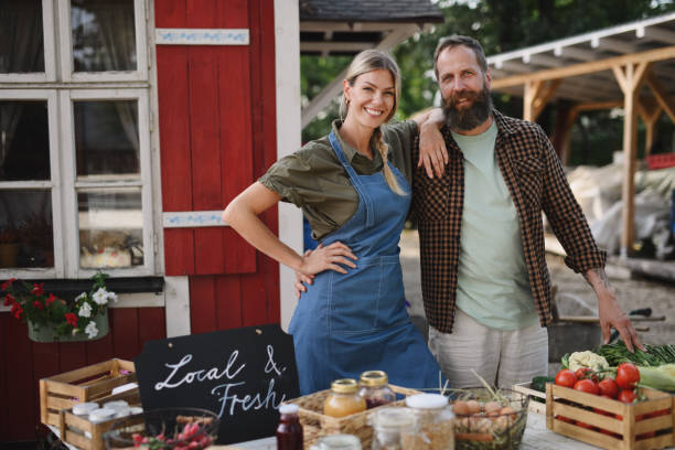 성숙한 부부 농민 지역 사회 농민 시장에서 자국 제품을 판매, 카메라를 보고. - farmers market market farmer community 뉴스 사진 이미지