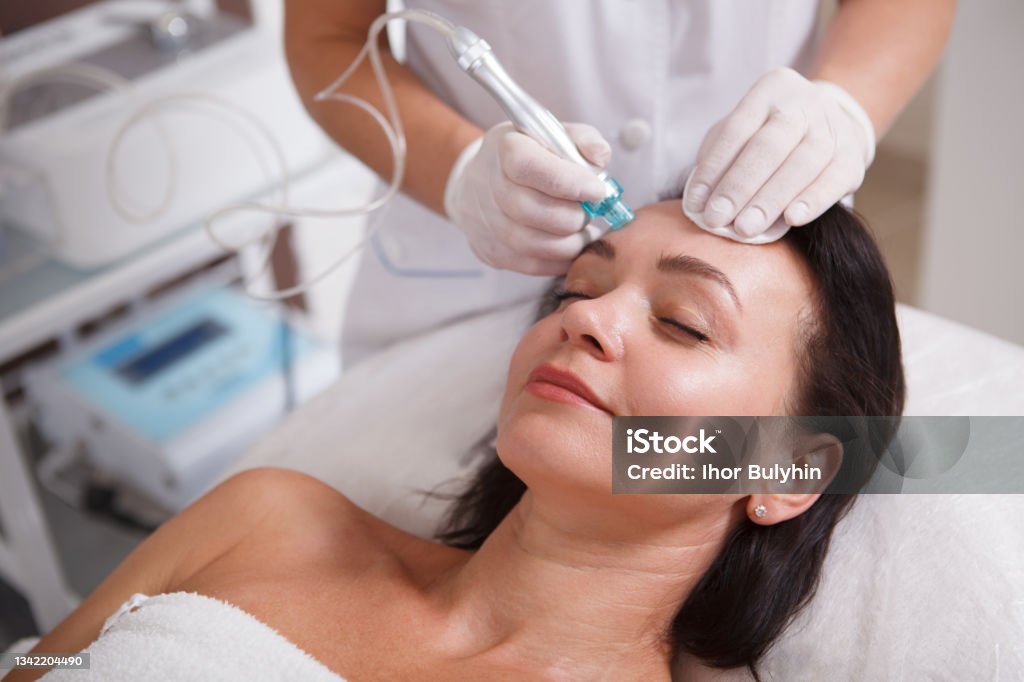 Mature woman getting skincare treatment at beauty clinic Mature woman enjoying getting Hydradermabrasian pore cleanse by beautician Facial Mask - Beauty Product Stock Photo