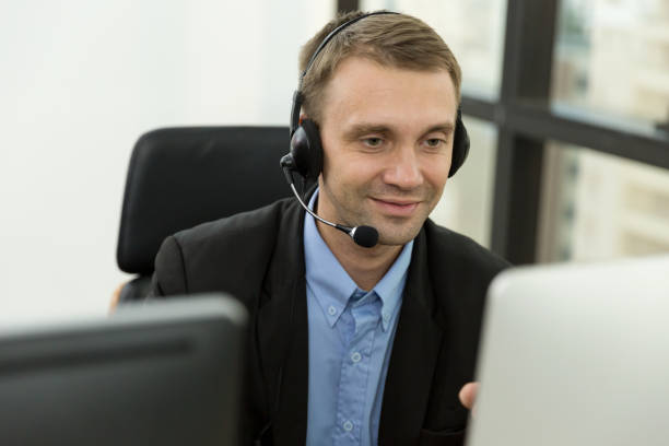 istock Call center male worker at work. Smiling male customer support operator in normal suit with headset working in the office. Contact center and customer service by headphone concept 1342204509