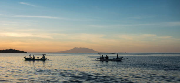 Sunset panoramic view of some traditional fishing boats along the coast in North Bali in Indonesia with Java volcano sitting over the horizon.