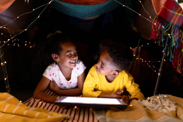 istock Happy african american siblings lying in makeshift tent, using tablet 1342207095