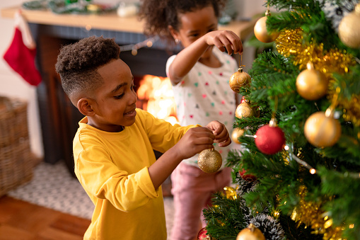 Happy african american siblings hanging baubles, decorating christmas tree. childhood, christmas, festivity and tradition at home.