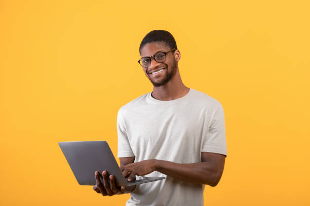 istock Excited black freelancer man using laptop, standing in studio over yellow background and smiling to camera, copy space 1342209838
