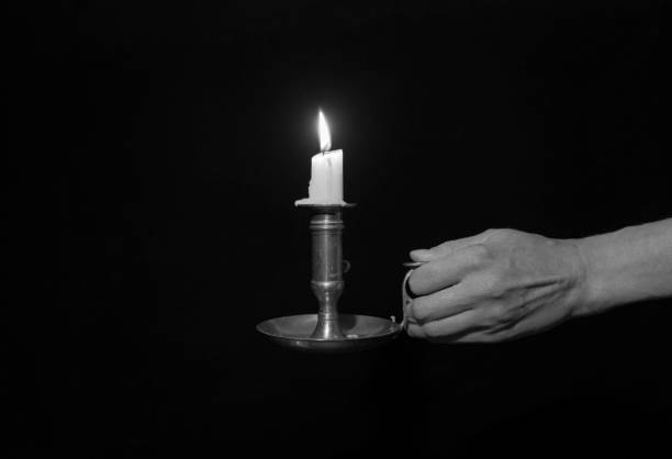 istock Decorative copper candlestick with burning candles in a female hand on a black background. Black and white 1342211525