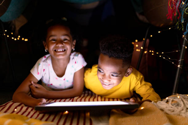istock Happy african american siblings lying in makeshift tent, using tablet 1342212434