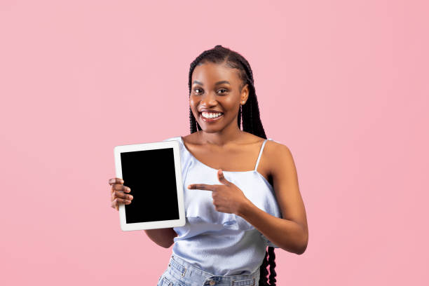 istock Positive young Afro woman pointing at tablet computer with empty screen on pink background, mockup for website or app 1342213223