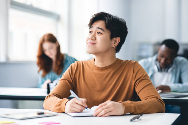 istock Smiling asian student sitting at desk in classroom looking away 1342216062