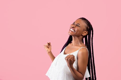 Emotional black lady with Afro bunches making YES gesture, feeling triumphant on pink studio background, copy space. Overjoyed African American woman celebrating success or achievement
