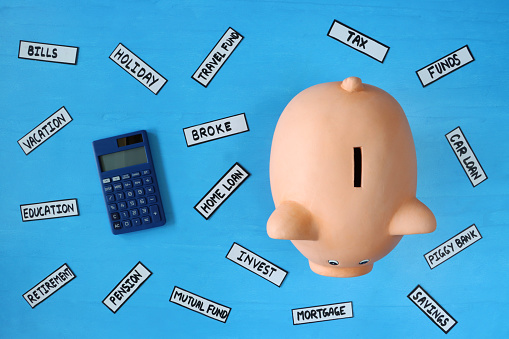 Stock photo showing an elevated view of piggy bank besides a calculator on a blue surface. This is a concept picture designed to suggest savings, mortgages, loans, home finances, wealth and the general cost of living.