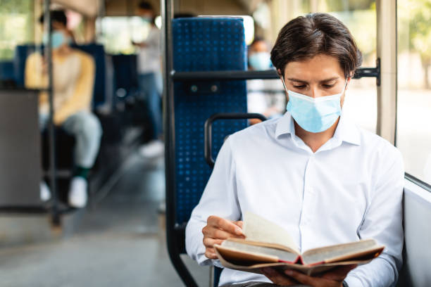 istock Focused man in mask reading book sitting at autobus 1342218980