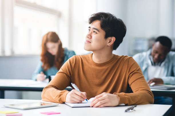 istock Smiling asian student sitting at desk in classroom thinking 1342222012