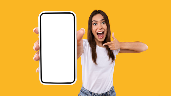Excited woman showing white empty smartphone screen and pointing