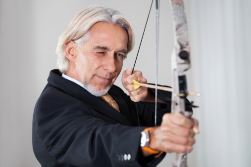 Portrait of successful businessman aiming at target with bow and arrow.