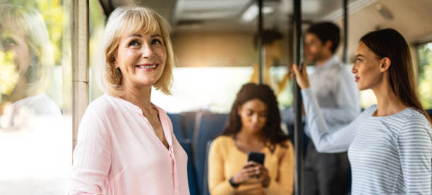 bella donna matura sorridente che prende l'autobus, guardando fuori dal finestrino - bus inside of people train foto e immagini stock