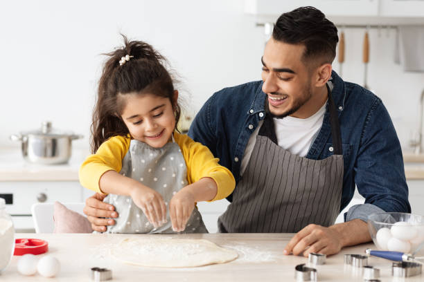 istock Cheerful arab dad and little daughter baking together in kitchen, making pizza 1342224291