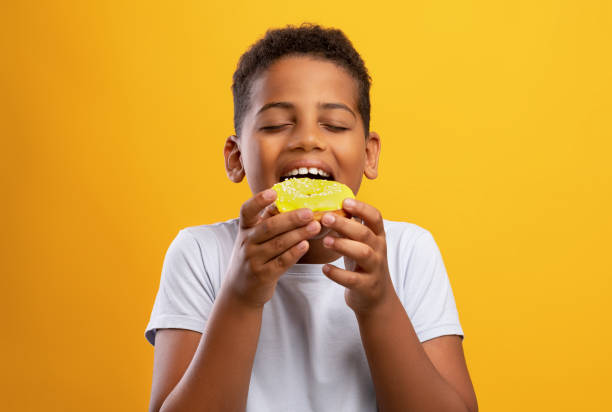 Black boy eating colorful donut, isolated on yellow background