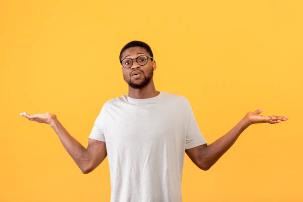 istock Confused black guy raising hands up and looking at camera, standing over yellow studio background 1342226248