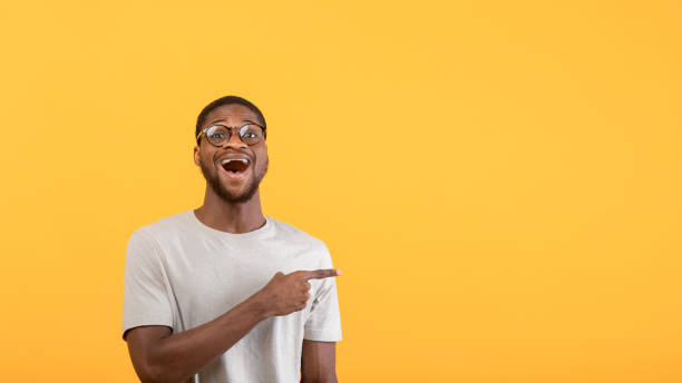 istock Unbelievable promo. Surprised black guy pointing aside at blank space on yellow studio background, panorama 1342226835