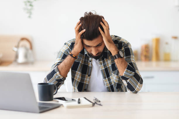 istock Depressed man sitting in front of laptop, touching his head 1342227030