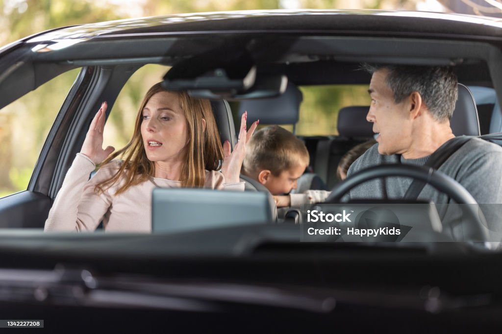 Frustrated parents arguing during trip by a car Angry parents arguing while traveling with their displeased kids in car during road trip. Car Stock Photo