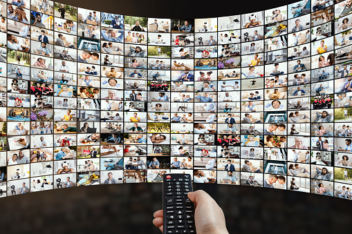 Broadcasting And Streaming Concept. Person holding remote control, switching channels or choosing movie, watching tv show. Multimedia and video on demand technology. Screen with thumbnails