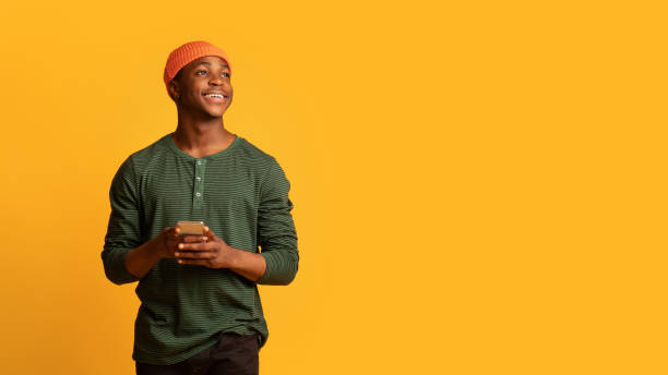 istock Dreamy Young Black Guy Holding Smartphone In Hands And Looking Aside 1342228989