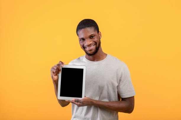 istock Young black guy showing digital tablet with blank screen, recommending website or mobile application, yellow background 1342229179