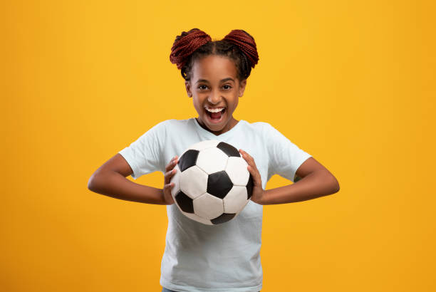 allegra ragazza afro-americana che tiene il pallone da calcio sul giallo - african descent child little girls african ethnicity foto e immagini stock