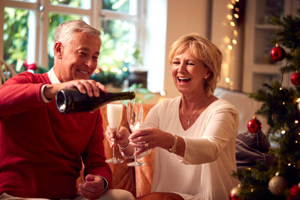 Loving Senior Couple Celebrating With Champagne Around Christmas Tree At Home stock photo