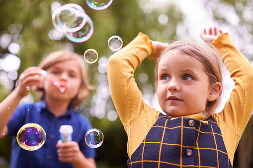 Boy And Girl Having Fun In Garden Blowing Bubbles Together