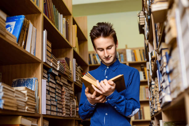 istock Male student in blue shirt with book in library 1342233593