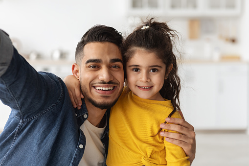 Closeup Shot Of Happy Middle Eastern Father Taking Selfie With His Little Daughter At Home, Cheerful Young Arab Dad And Cute Little Female Kid Embracing And Smiling At Camera Together, Free Space