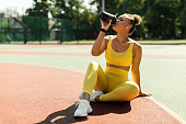 Portrait of sporty black woman in yellow sportswear drinking water