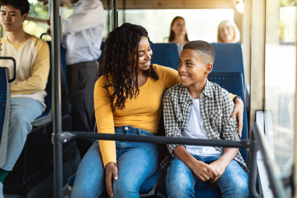 Beautiful smiling African American family going on a bus Happy Family On The Bus. Portrait of smiling young African American woman and boy sitting and going on a public transport, lady hugging son and looking at each other, enjoying ride or travel riding stock pictures, royalty-free photos & images